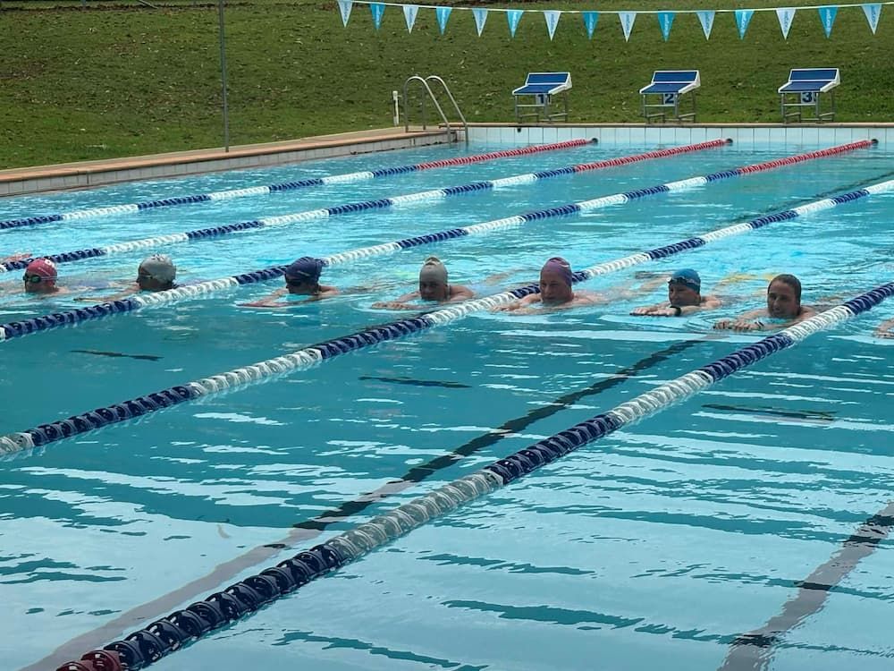 Six Swimmers Wearing Caps Swim in Lanes in an Outdoor Pool — Cannonvale Swim Centre In Cannonvale, QLD