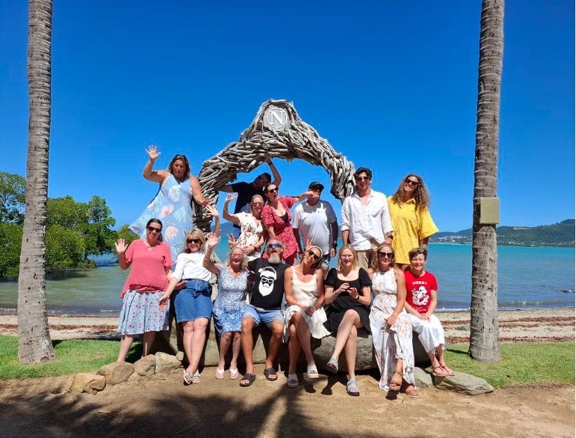 Group of people posing under a driftwood arch on a sunny beach with blue sky and water — Cannonvale Swim Centre In Cannonvale, QLD