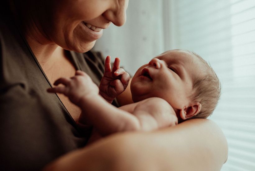 A postpartum mother is holding her newborn baby in her arms.