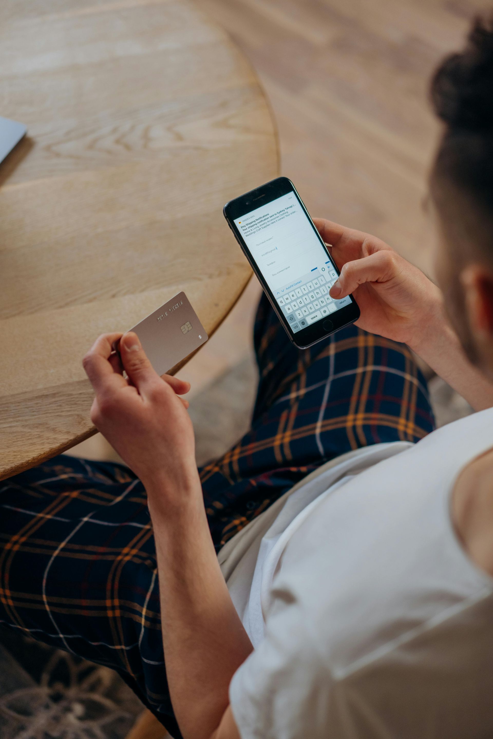 A man is sitting at a table holding a credit card and a cell phone.
