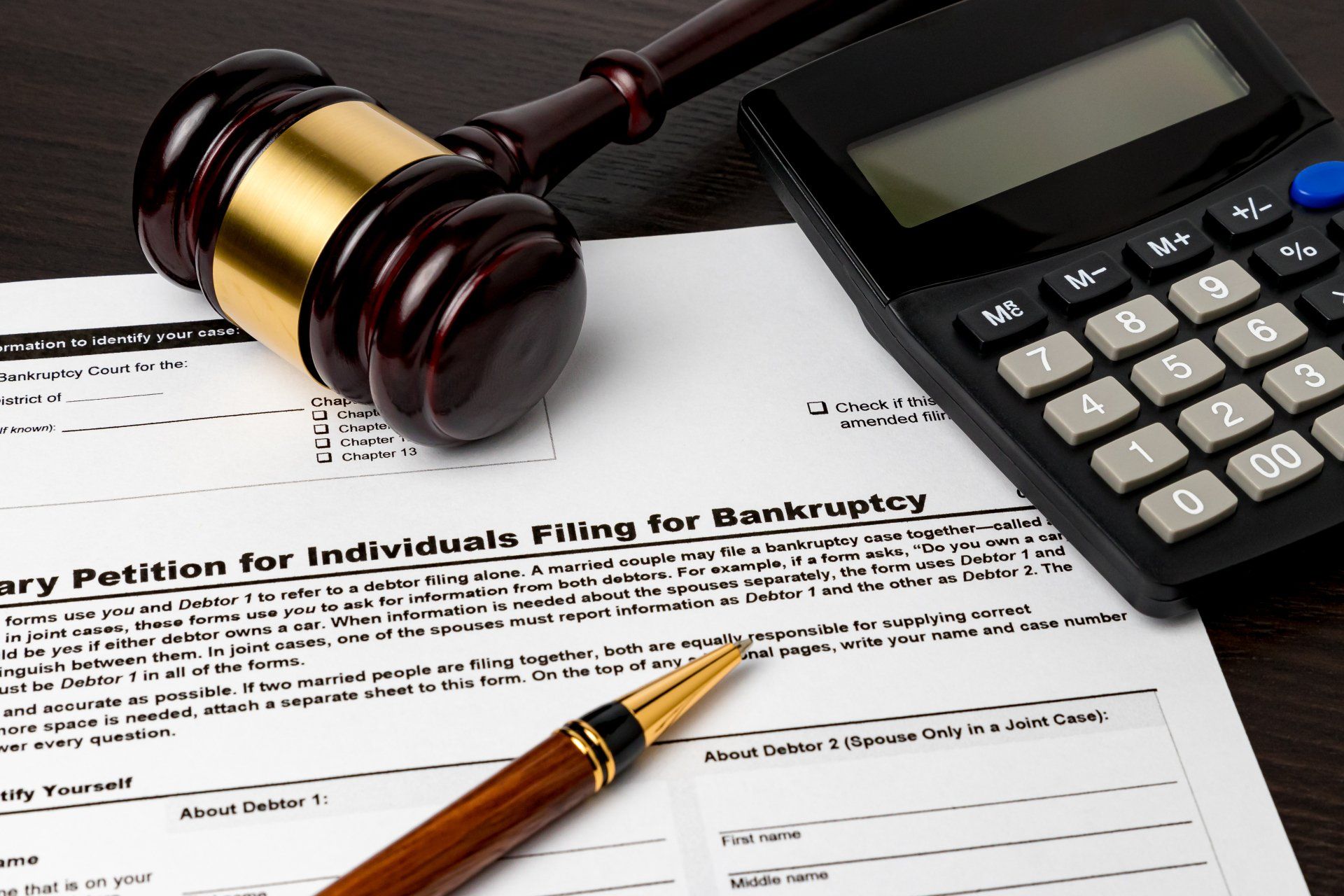 A calculator and a judge 's gavel on top of a petition for individual filing for bankruptcy