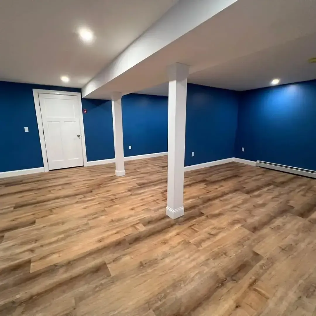 An empty basement with blue walls and wooden floors.