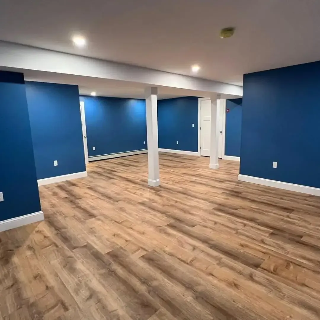 An empty basement with blue walls and wooden floors.