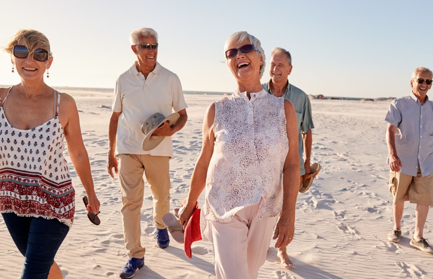 Group of smiling seniors walking on a beach in the sun; happy expressions.