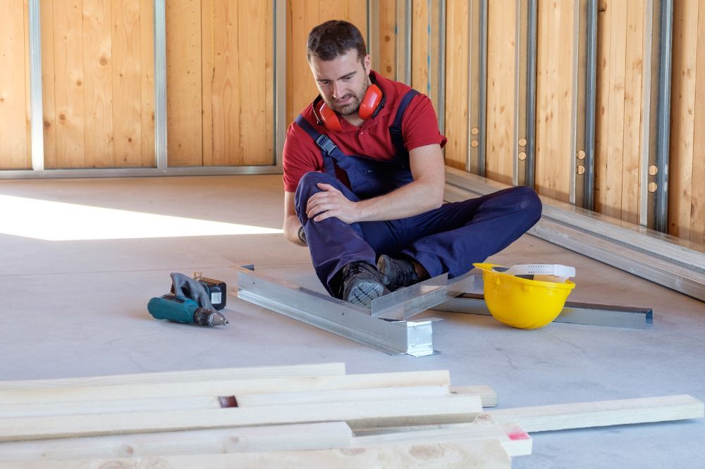 Construction worker sitting, injured knee, inside building under construction.