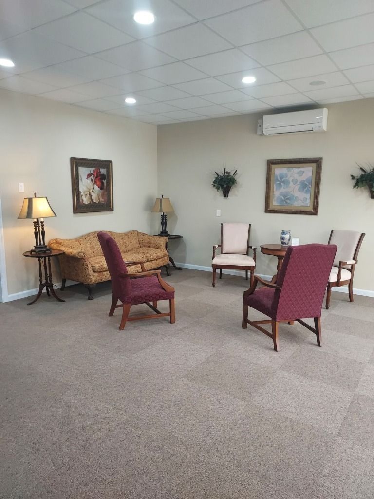 Cozy waiting room with mauve chairs, sofa, lamp, framed art, carpet, and wall air conditioner.