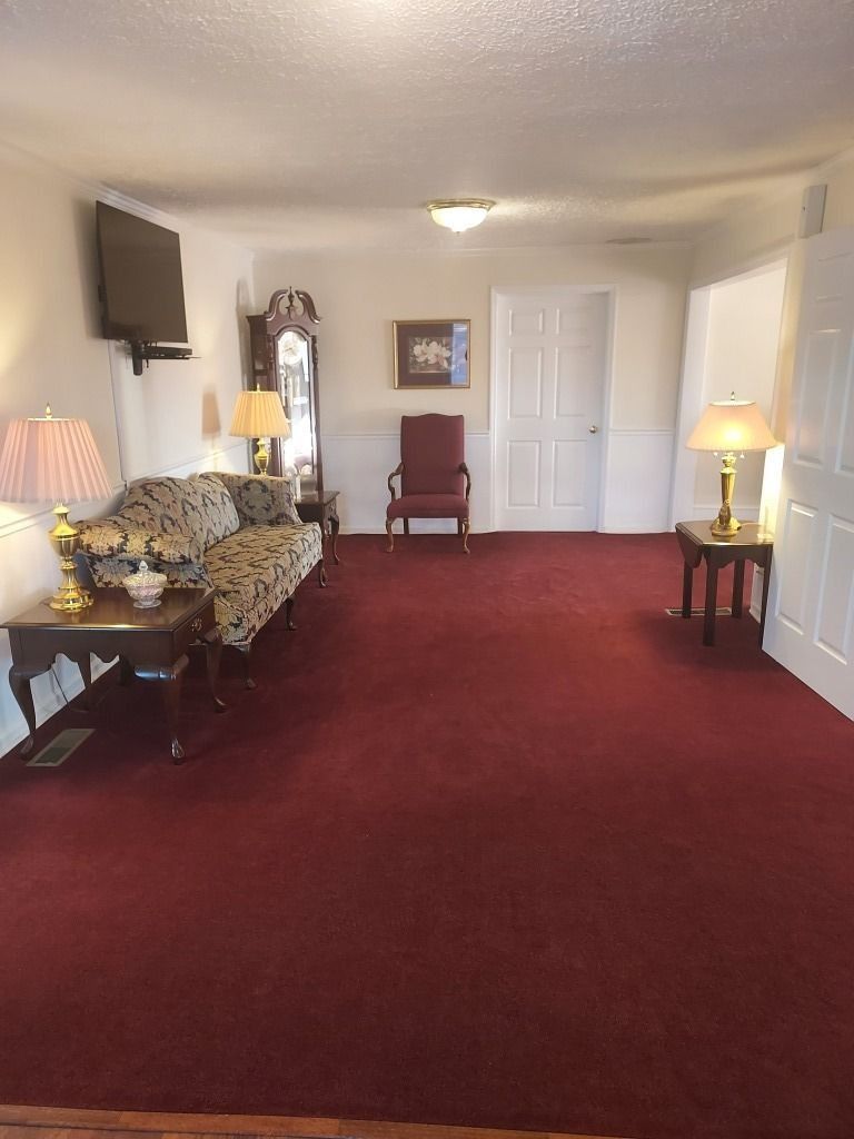 Empty living room with red carpet, white walls, floral sofa, and lamps on both sides