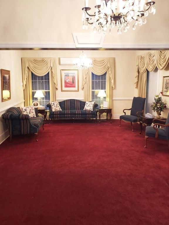 Elegant sitting room with red carpet, cream walls, chandelier, sofa, chairs, and framed art.