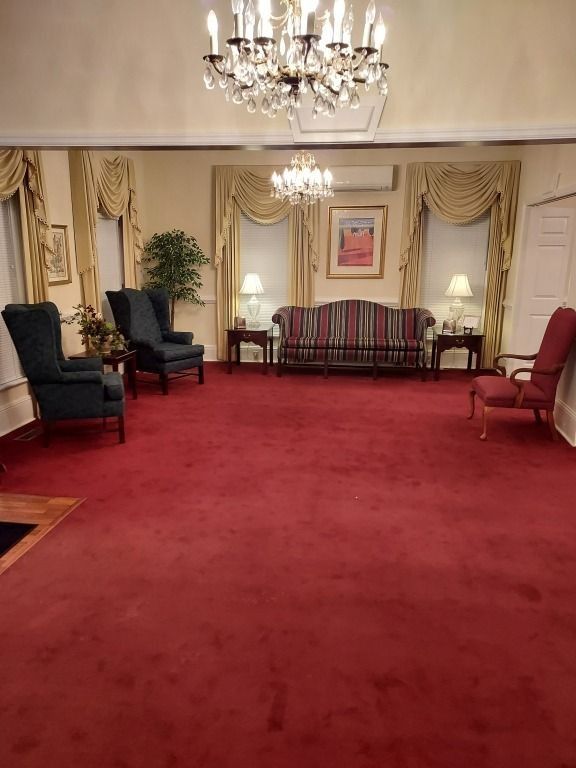 Elegant room with red carpet, chandeliers, striped sofa, and dark armchairs along the walls