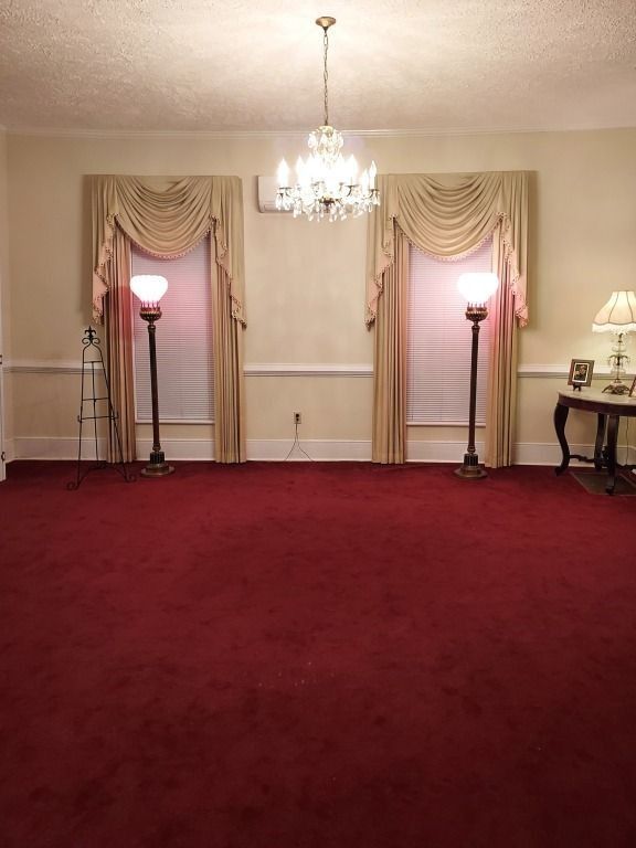 Elegant room with red carpet, cream drapes, chandelier, and two floor lamps against the back wall