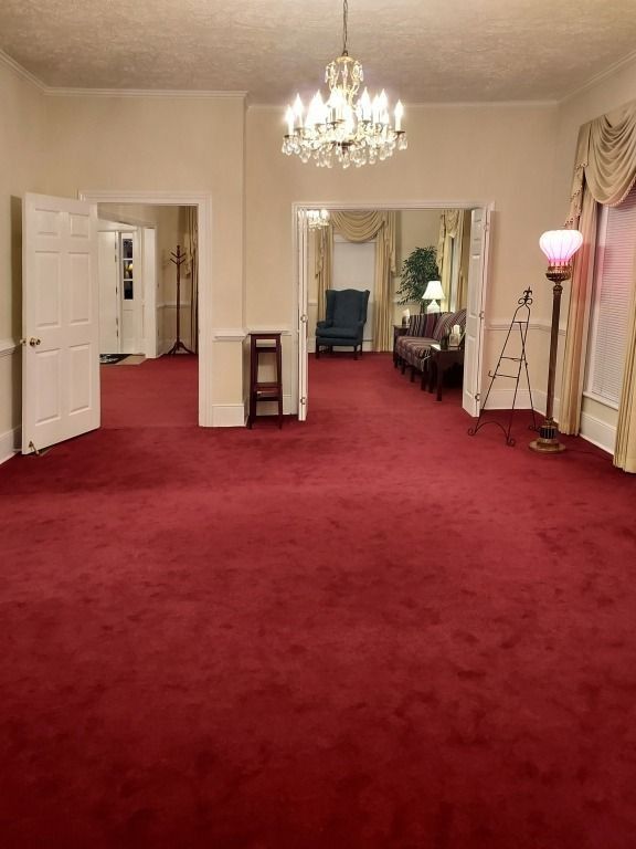 Elegant room with red carpet, chandelier, mirror, and white walls.