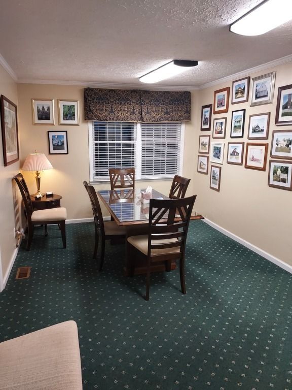 Small meeting room with a table, four chairs, framed photos, and a window with a valance.
