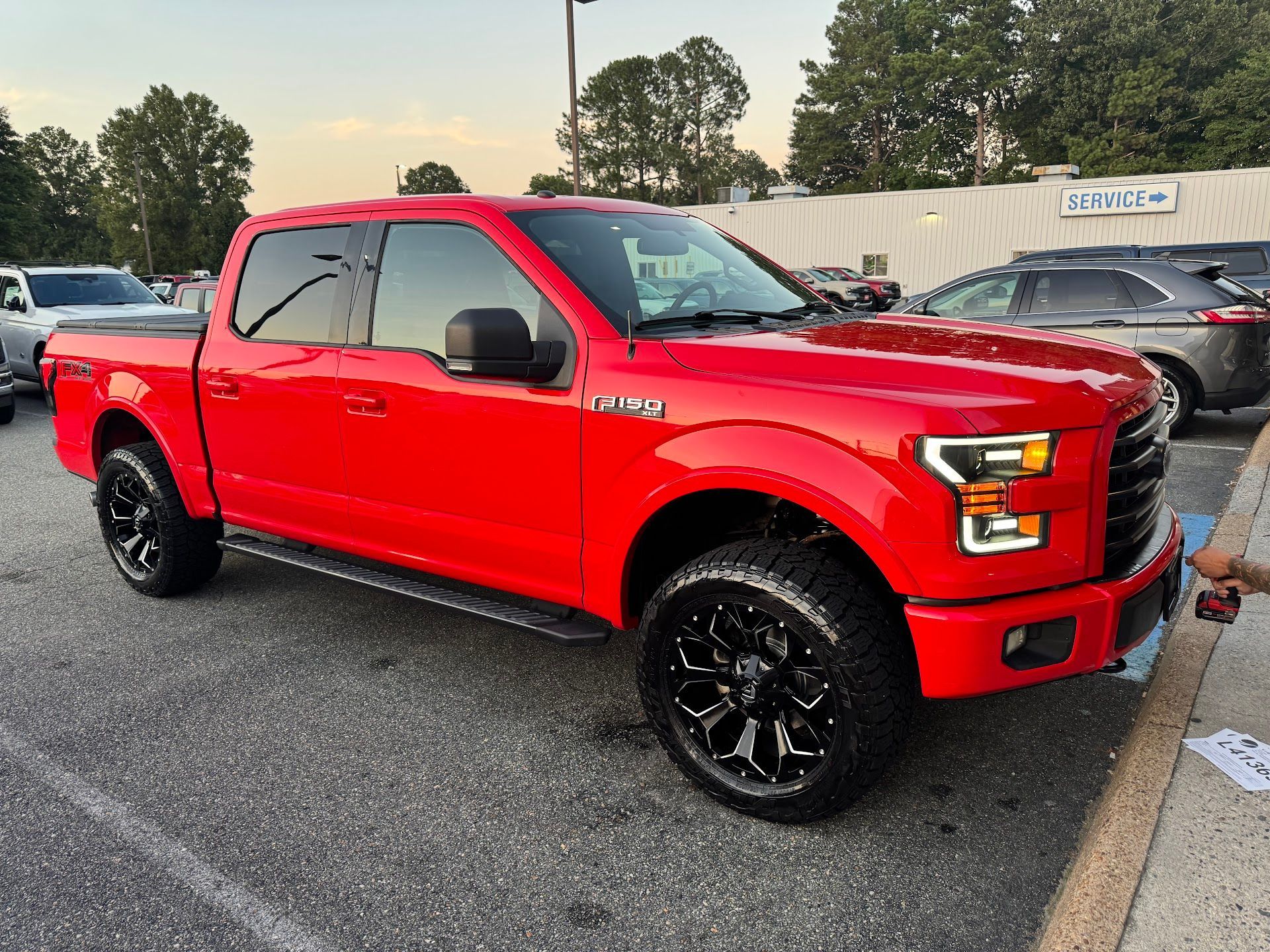 A bright red Ford F-150 crew cab pickup truck with black aftermarket wheels parked in a parking lot. | Sprinkle and Williams II, Inc.