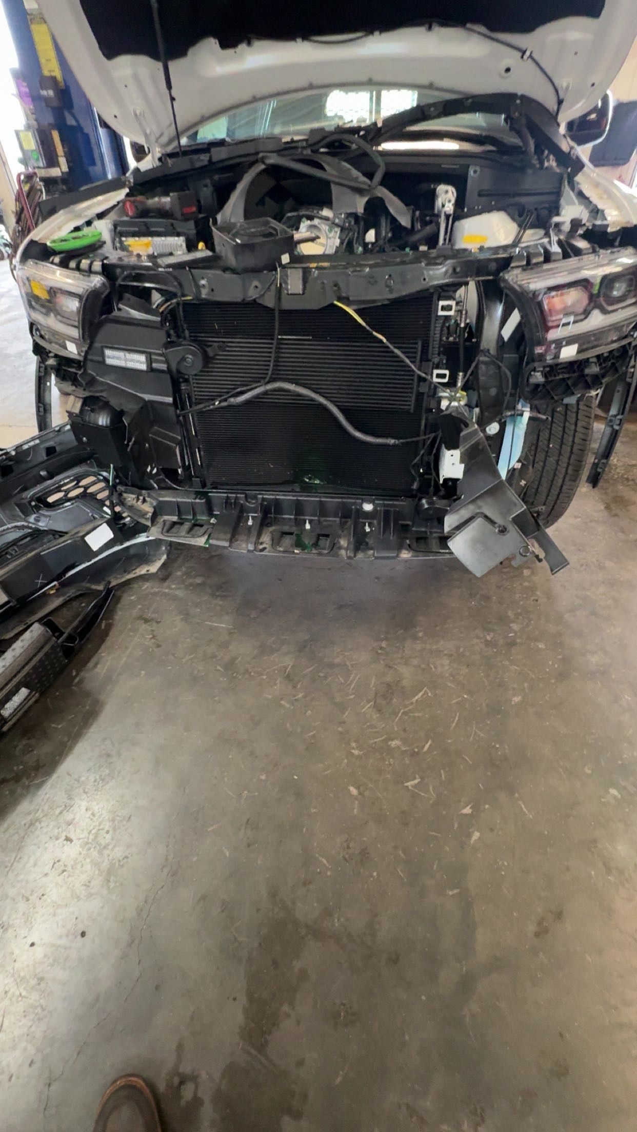 Severely damaged car front with hood open in a garage, exposed engine and broken bumper.