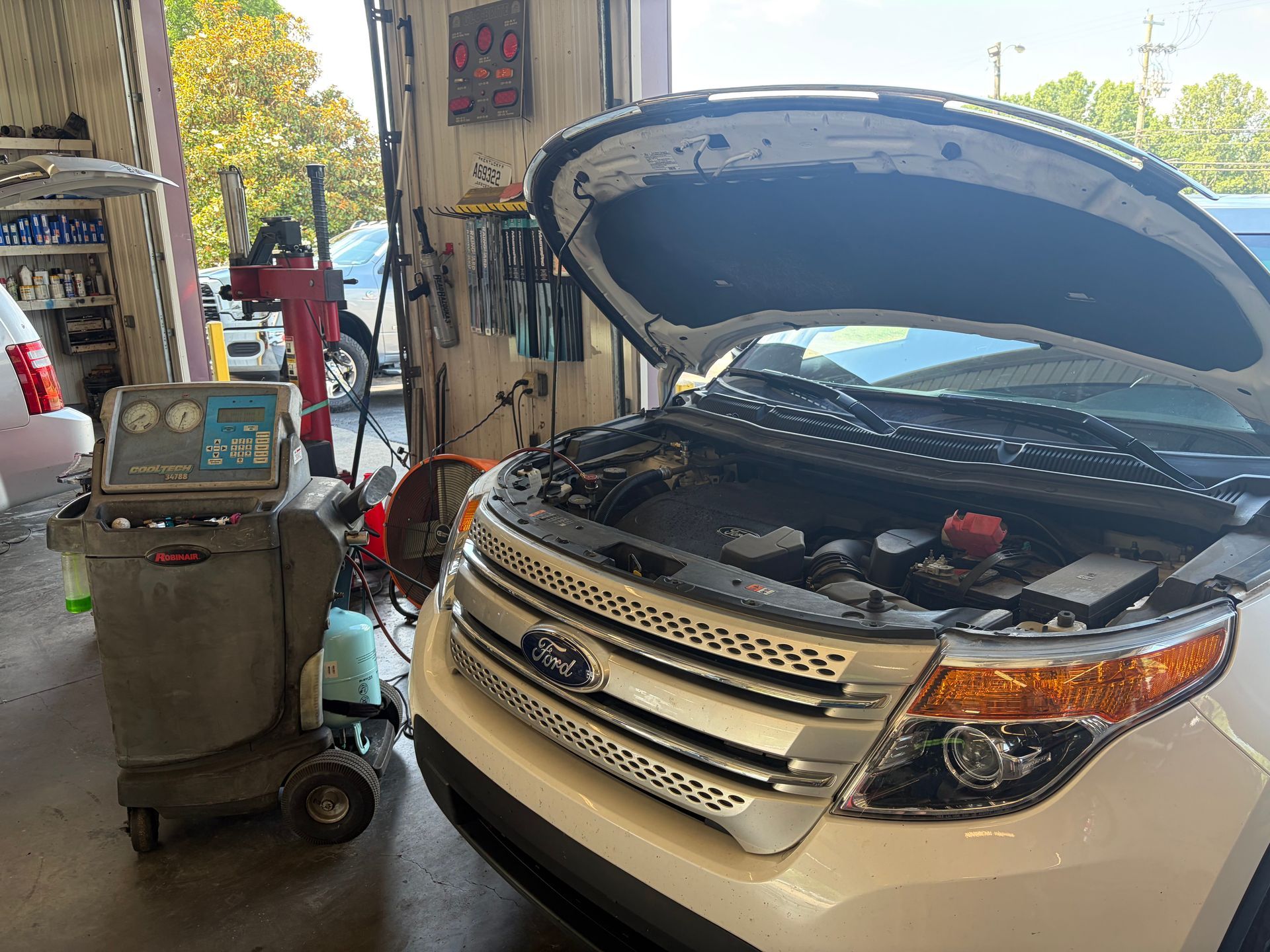 White SUV with hood open in a garage, next to a diagnostic cart and equipment