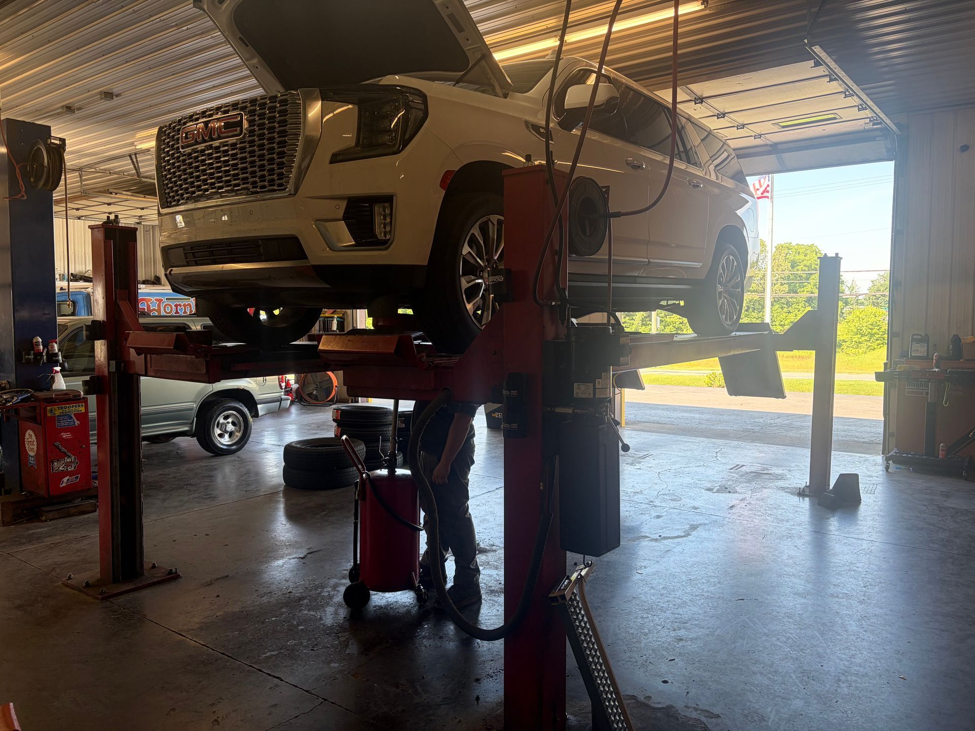 White SUV on a lift in an auto repair shop, with tools and another car in the background.
