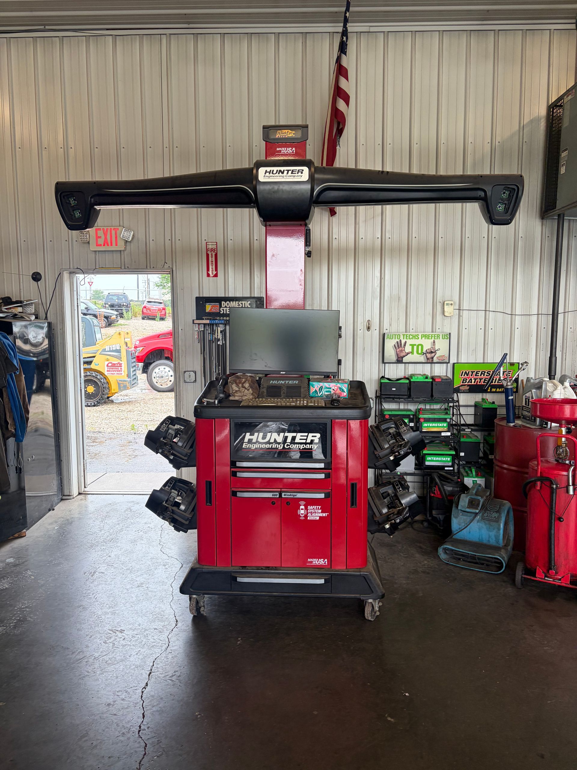 Red vehicle alignment machine in an auto shop with raised arms and a monitor, surrounded by tools and equipment.