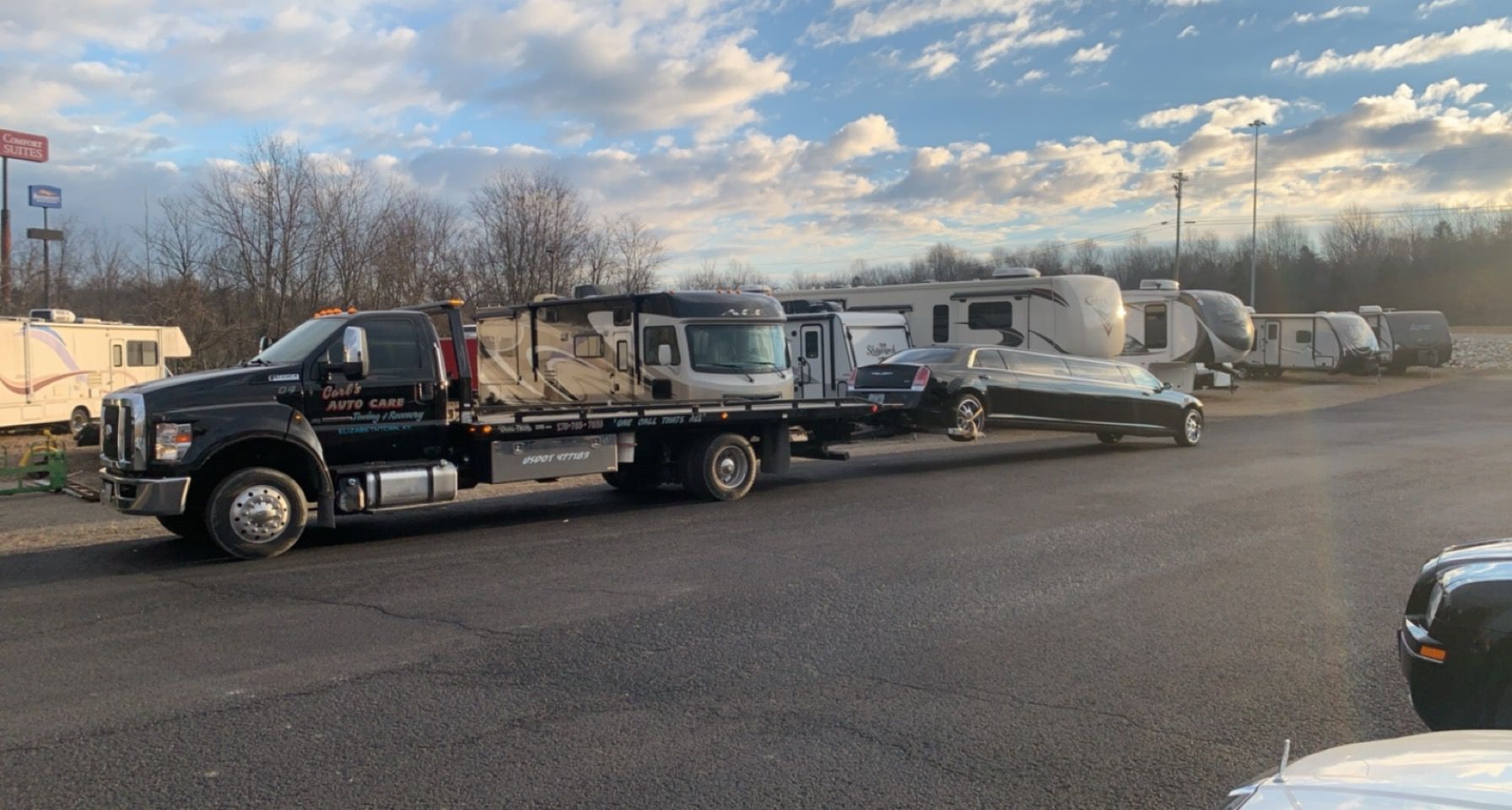 Tow truck hauling several white RVs parked along a roadside under a cloudy sky