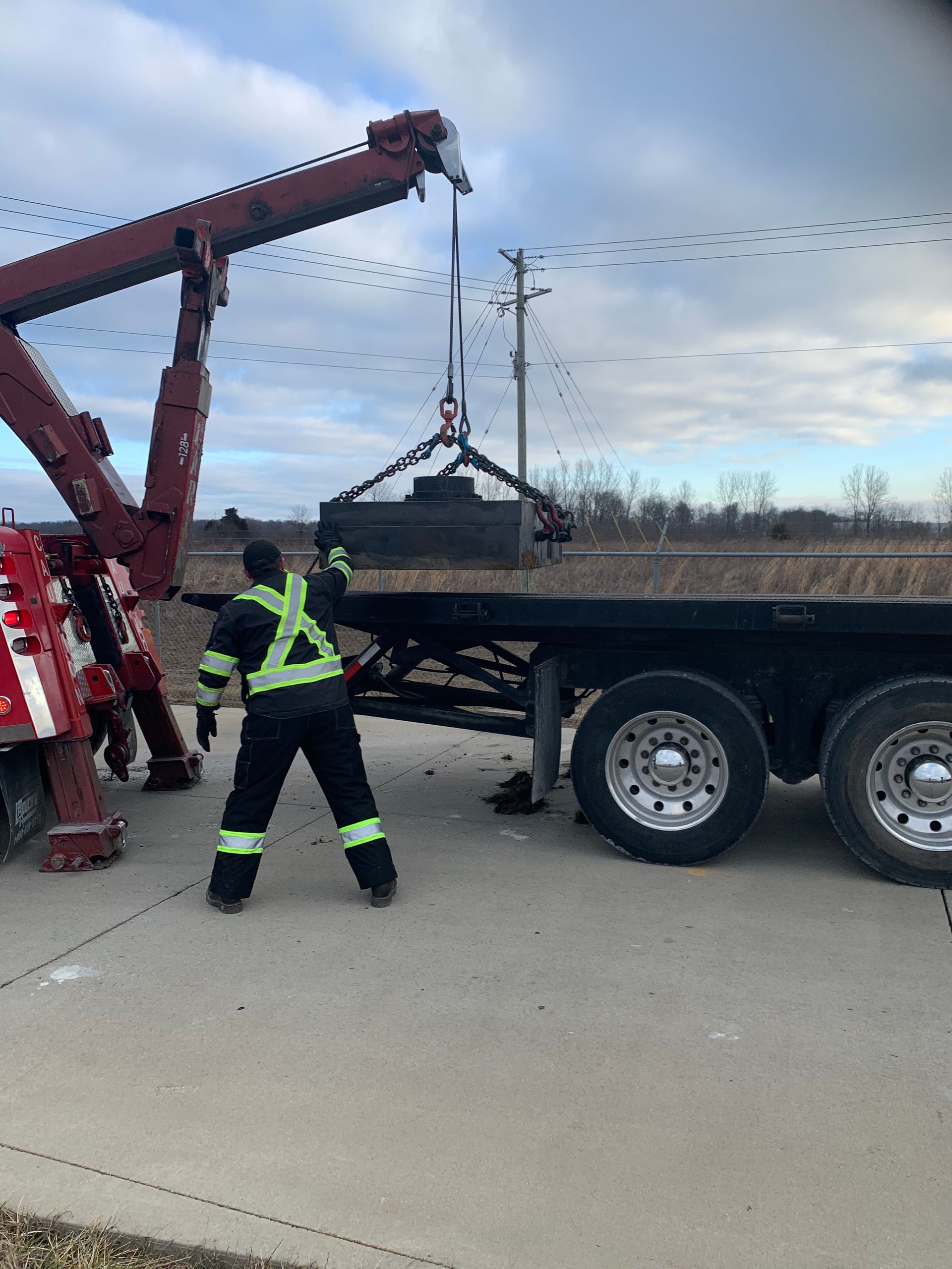Tow truck operator lifting a large metal object onto a flatbed truck on a roadside