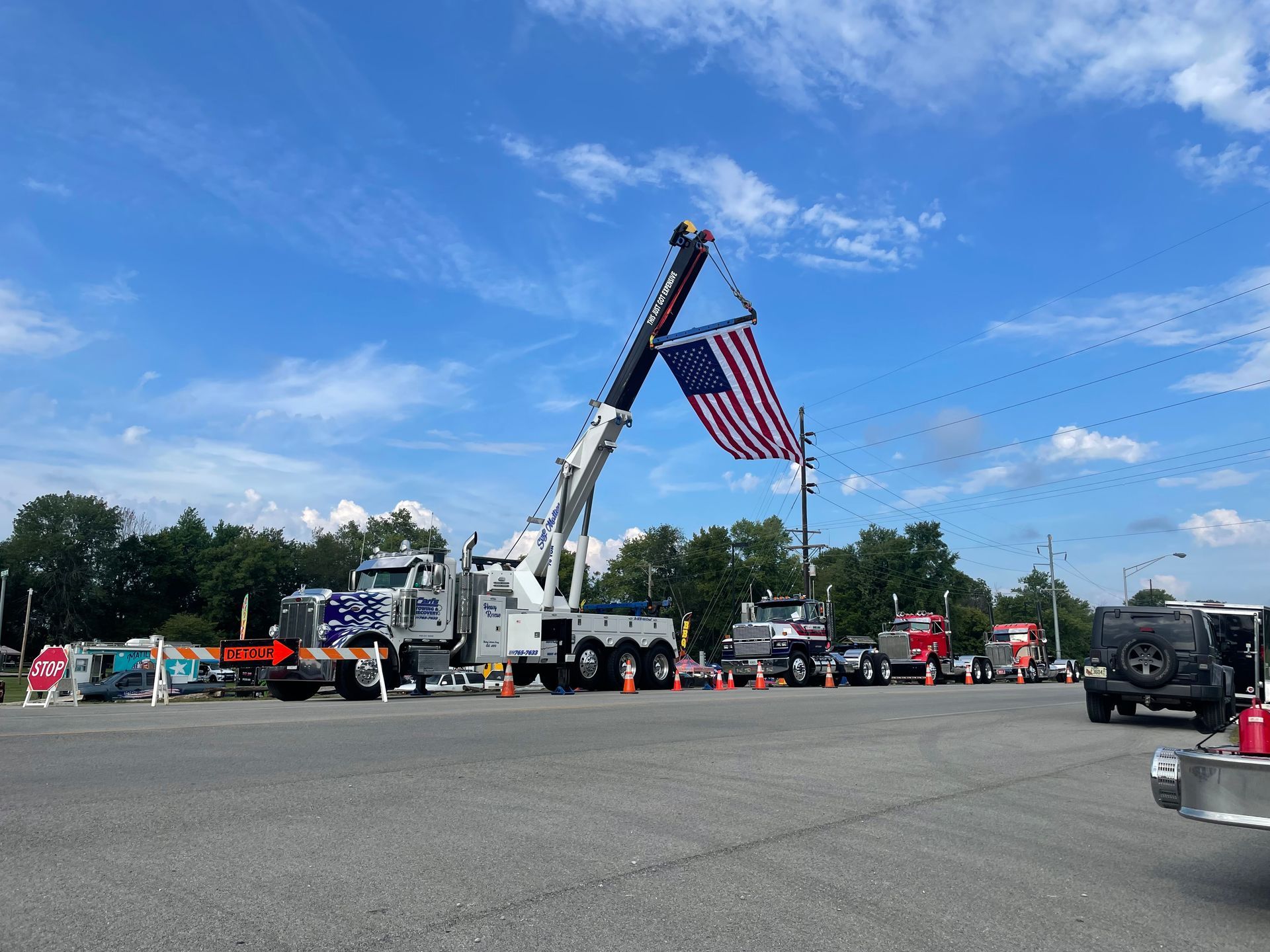 Tow truck raising a large American flag at an outdoor event under a blue sky