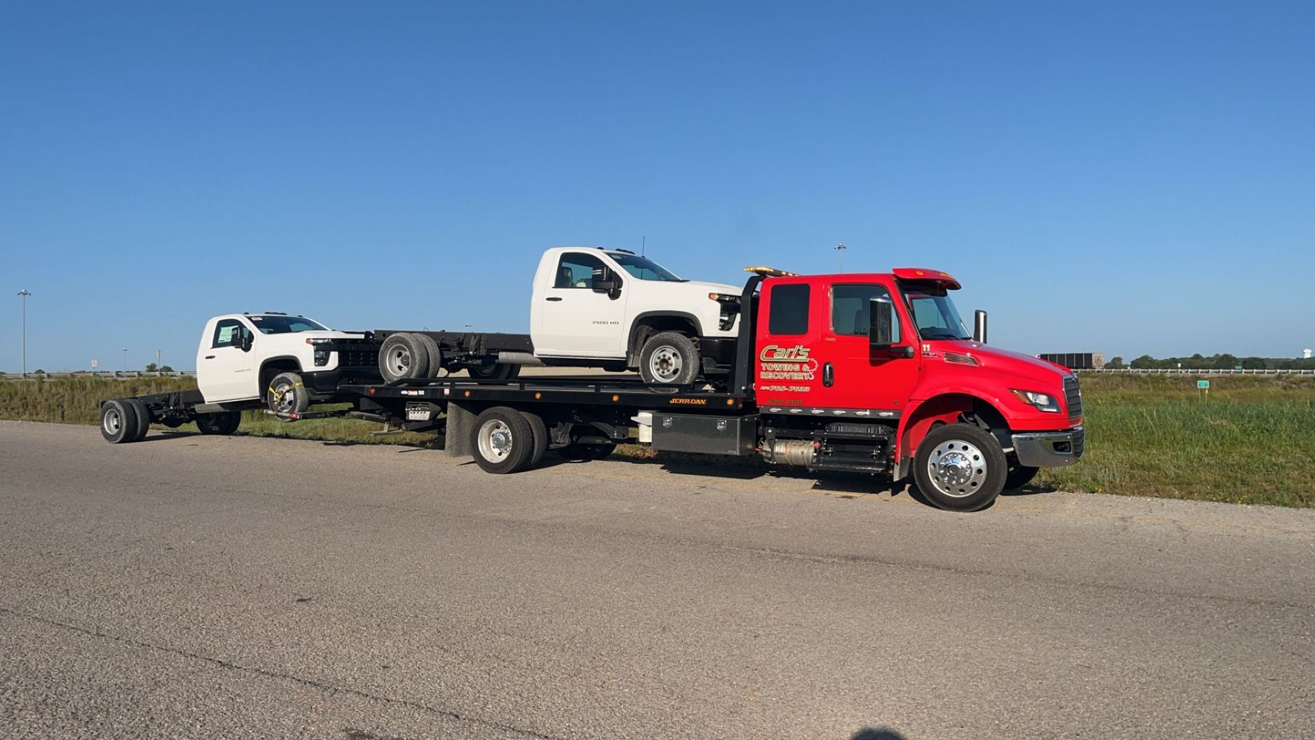 Tow truck hauling two wrecked vehicles on a roadside under a clear blue sky
