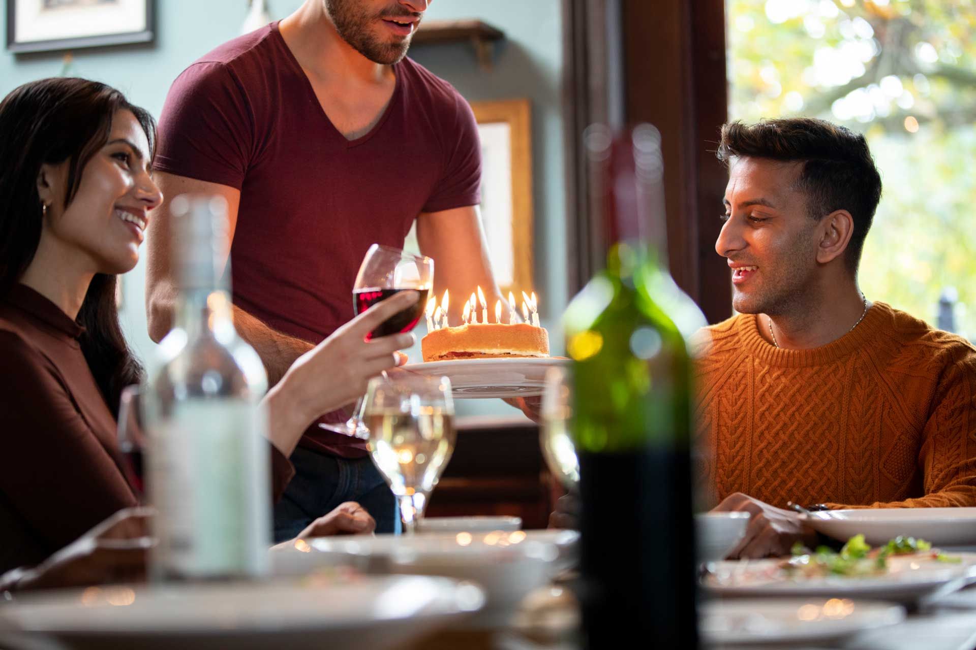 A man is serving a birthday cake to a group of people at a restaurant.