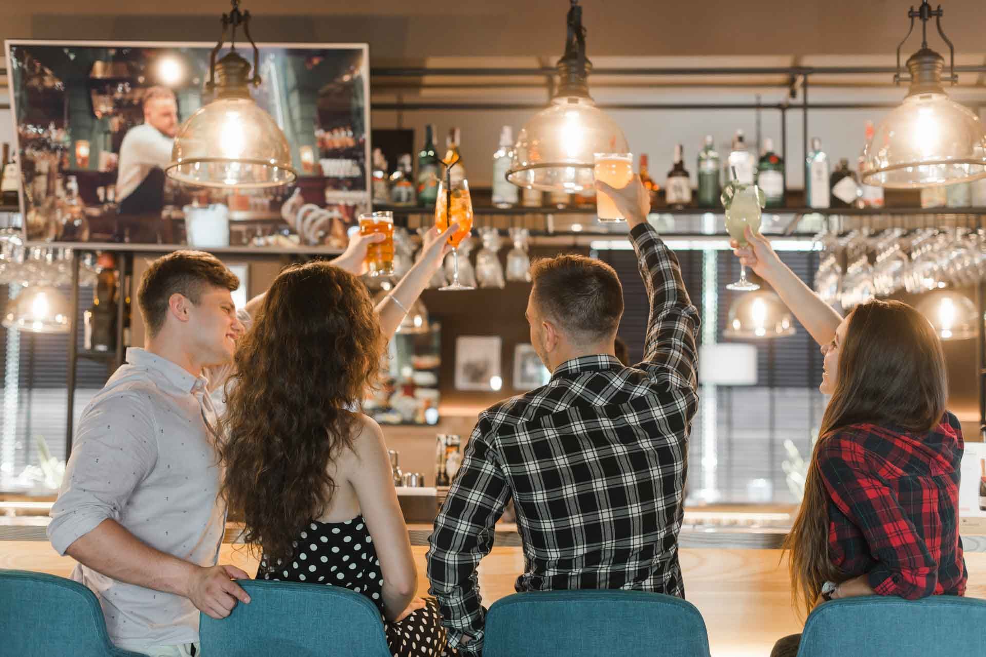A group of people are sitting at a bar raising their glasses in the air.