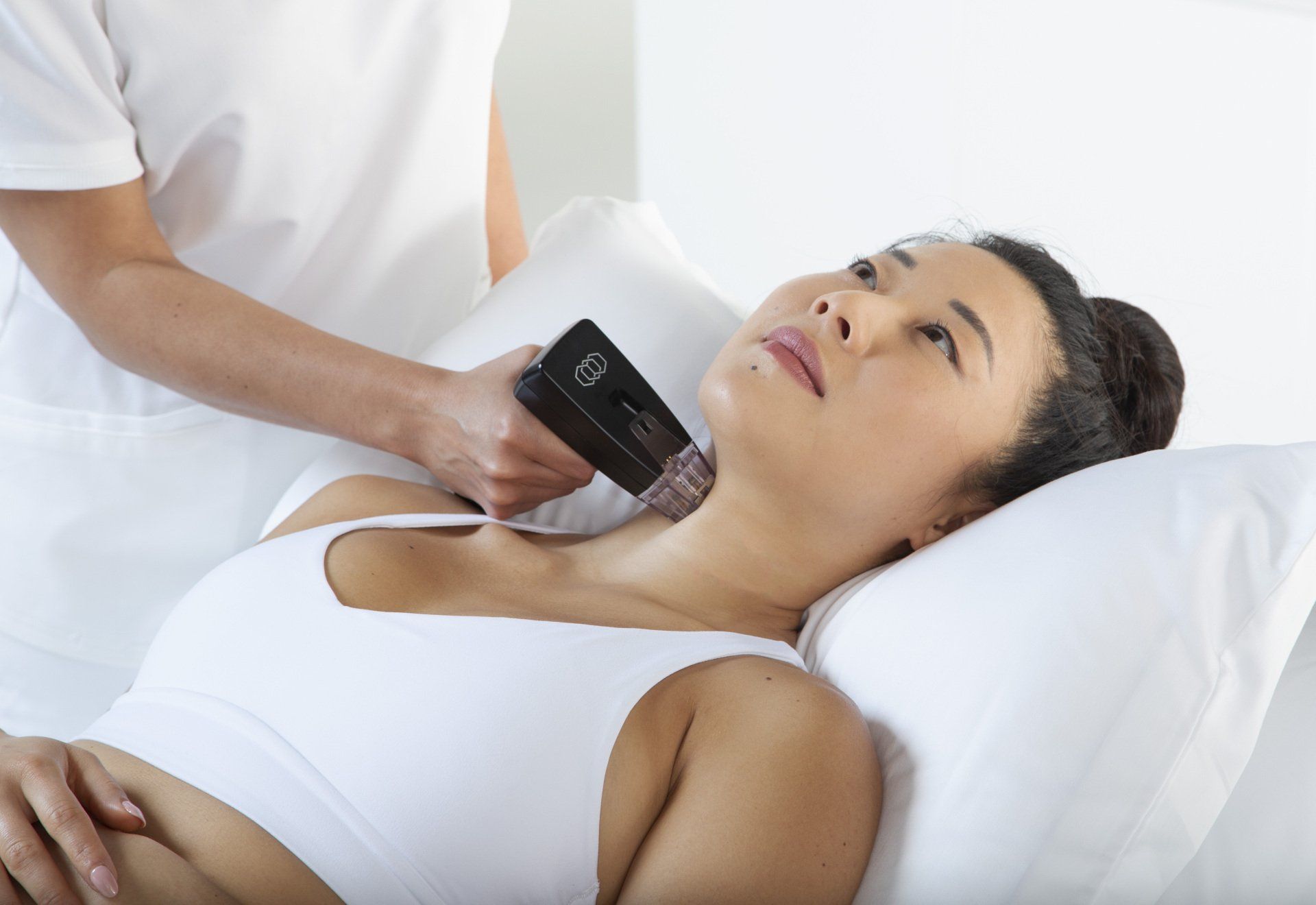 Person receiving a skin treatment on the neck. A practitioner holds a device. The setting is indoors.