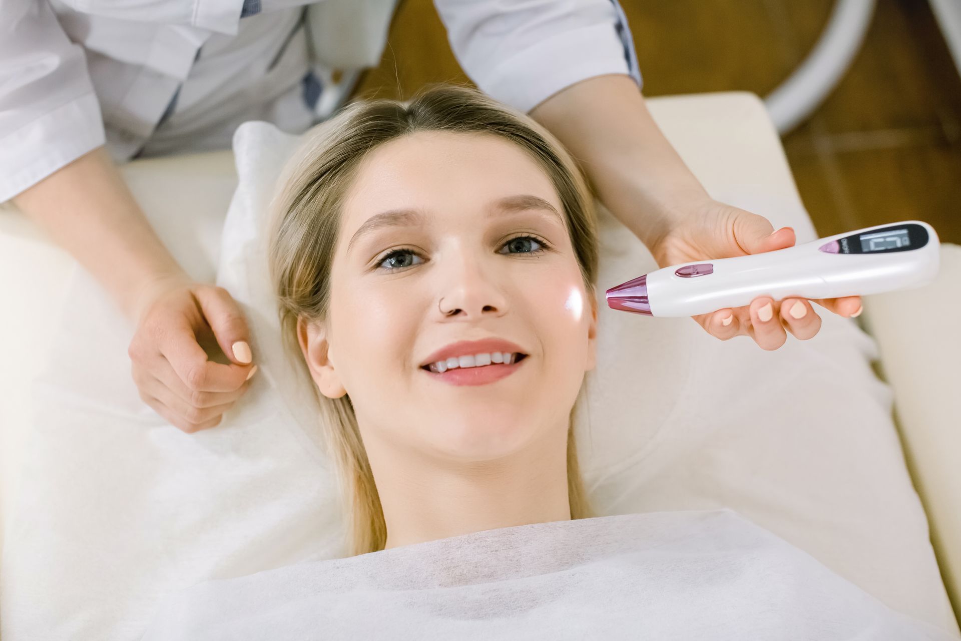 Woman receiving facial skin treatment from a person in a white coat.
