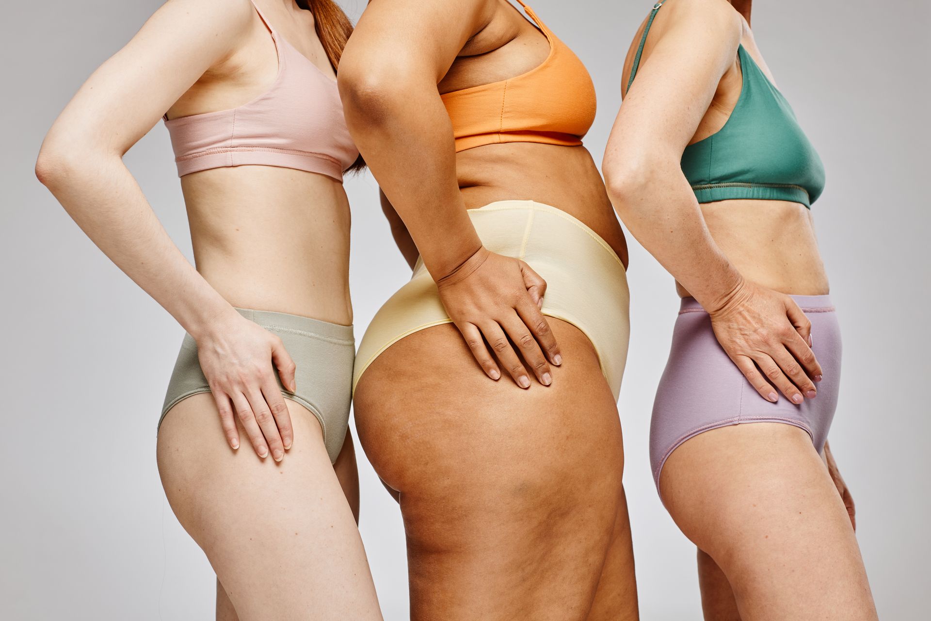 Three people in underwear pose, in profile, different body types and skin tones, hands on hips.