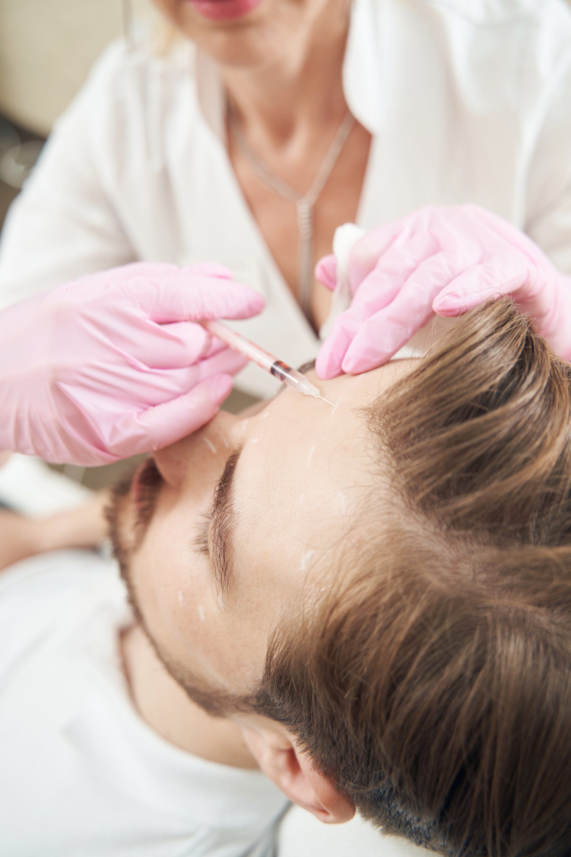 Person receiving an injection in the forehead from someone wearing pink gloves; in a medical setting.