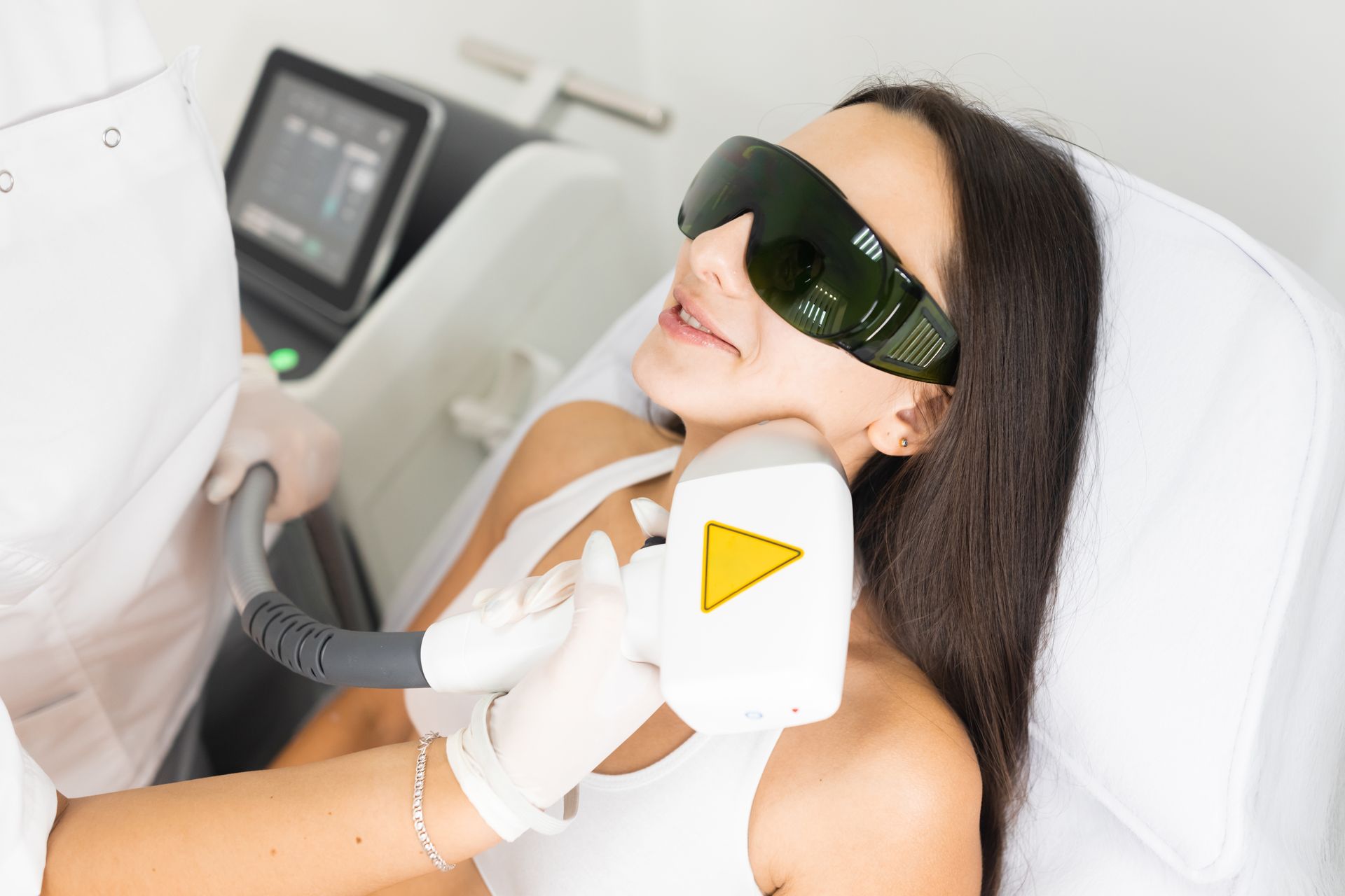 Woman receiving laser hair removal treatment on her neck; wearing protective eyewear.