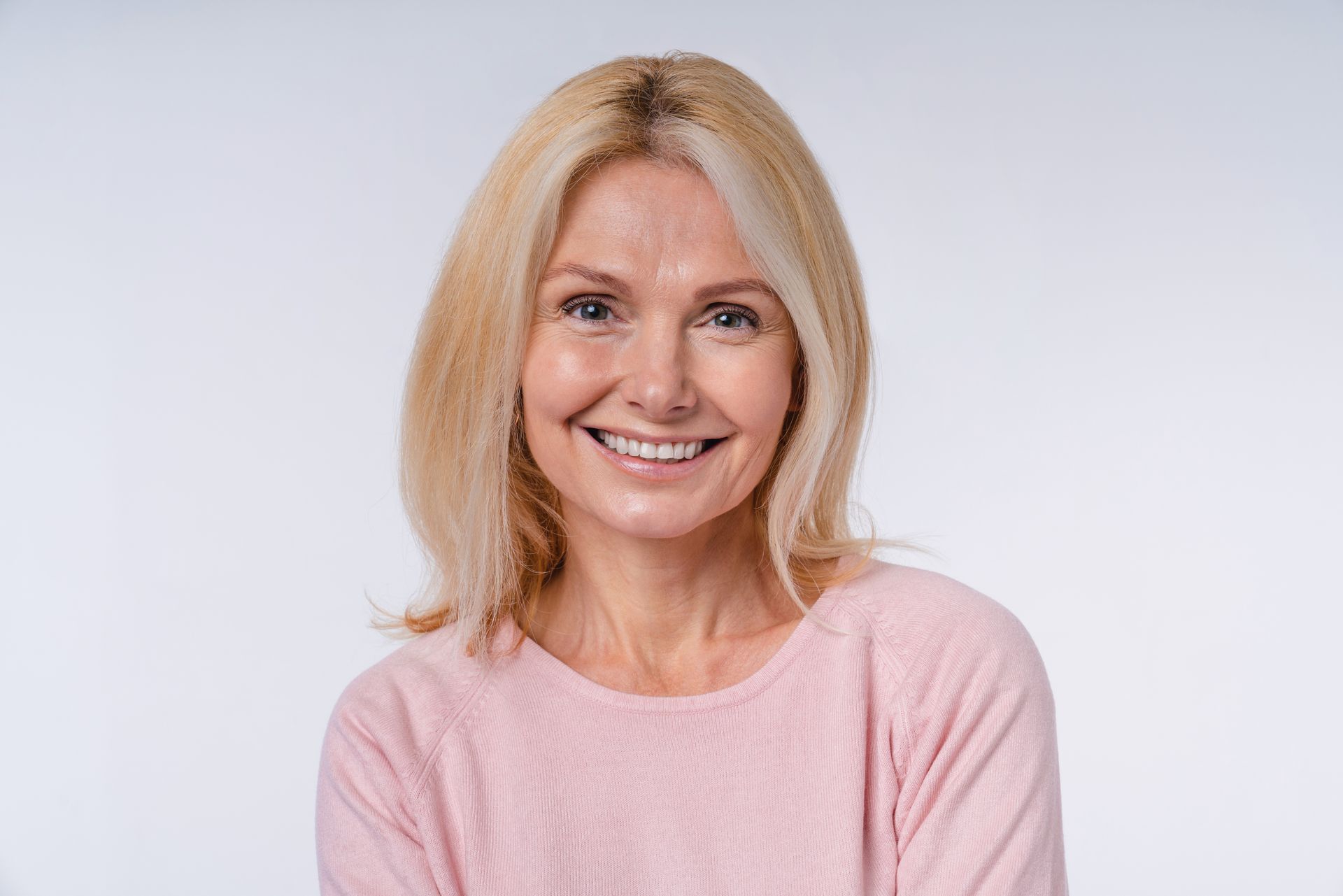 Woman with blond hair smiles at the camera, wearing a pink sweater, against a white backdrop.