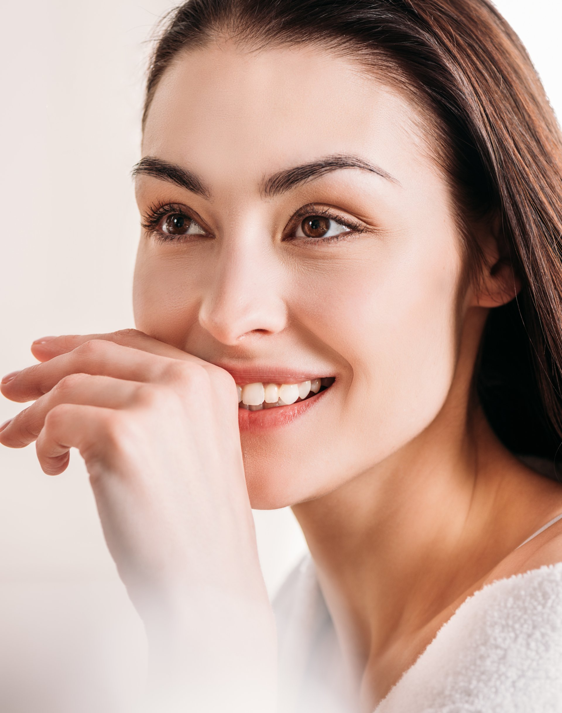 Woman smiling, hand near mouth. Brown hair, light skin, white background.