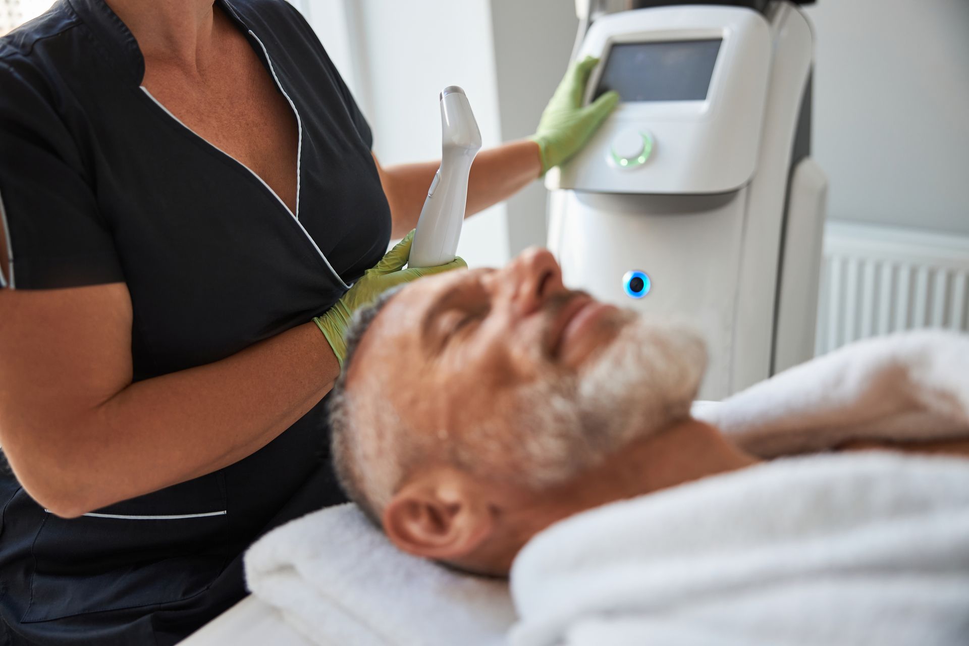 Man receiving facial treatment from a technician using a device in a medical setting.