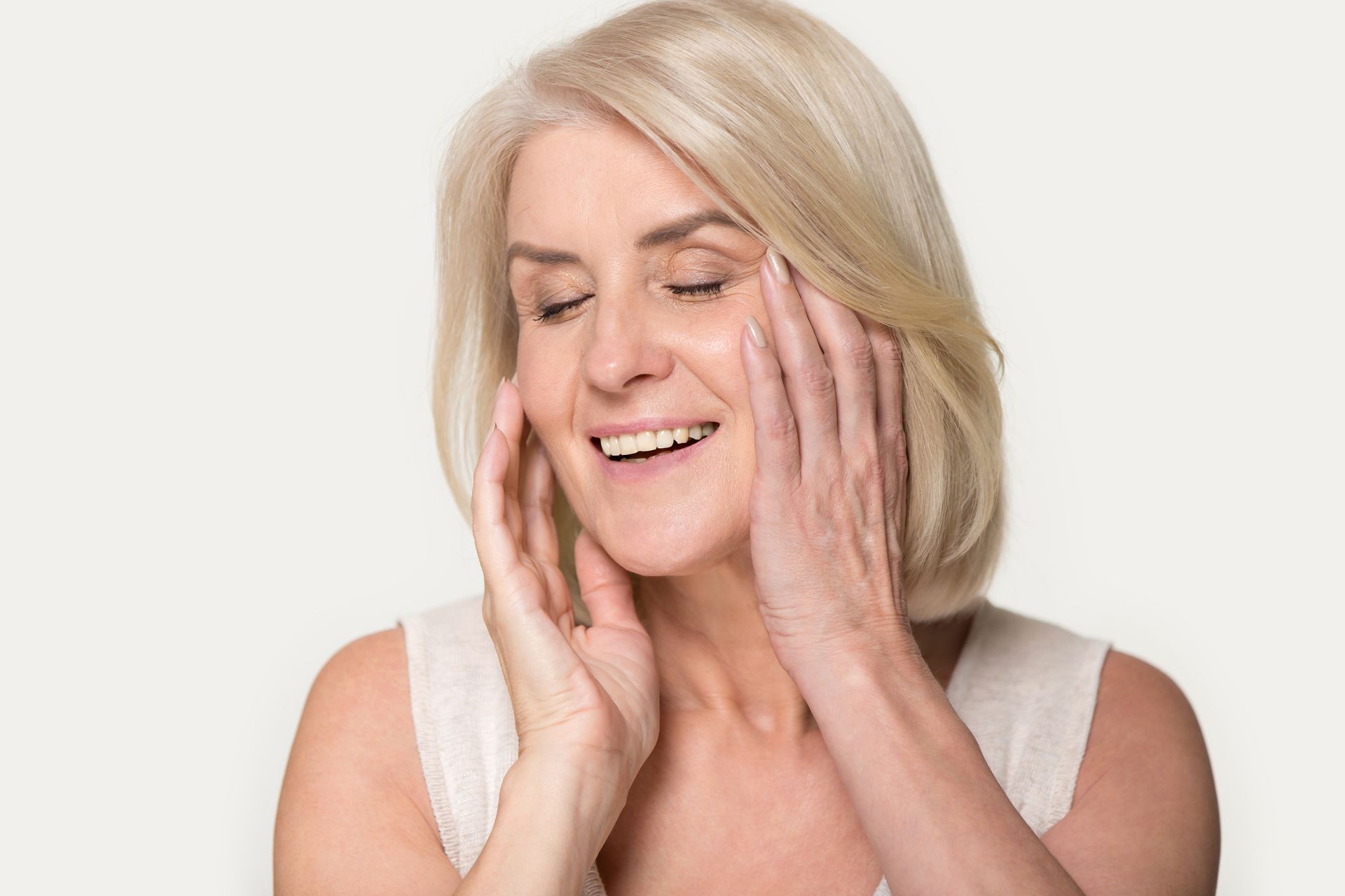 Woman with blonde hair smiling, touching her face, eyes closed.