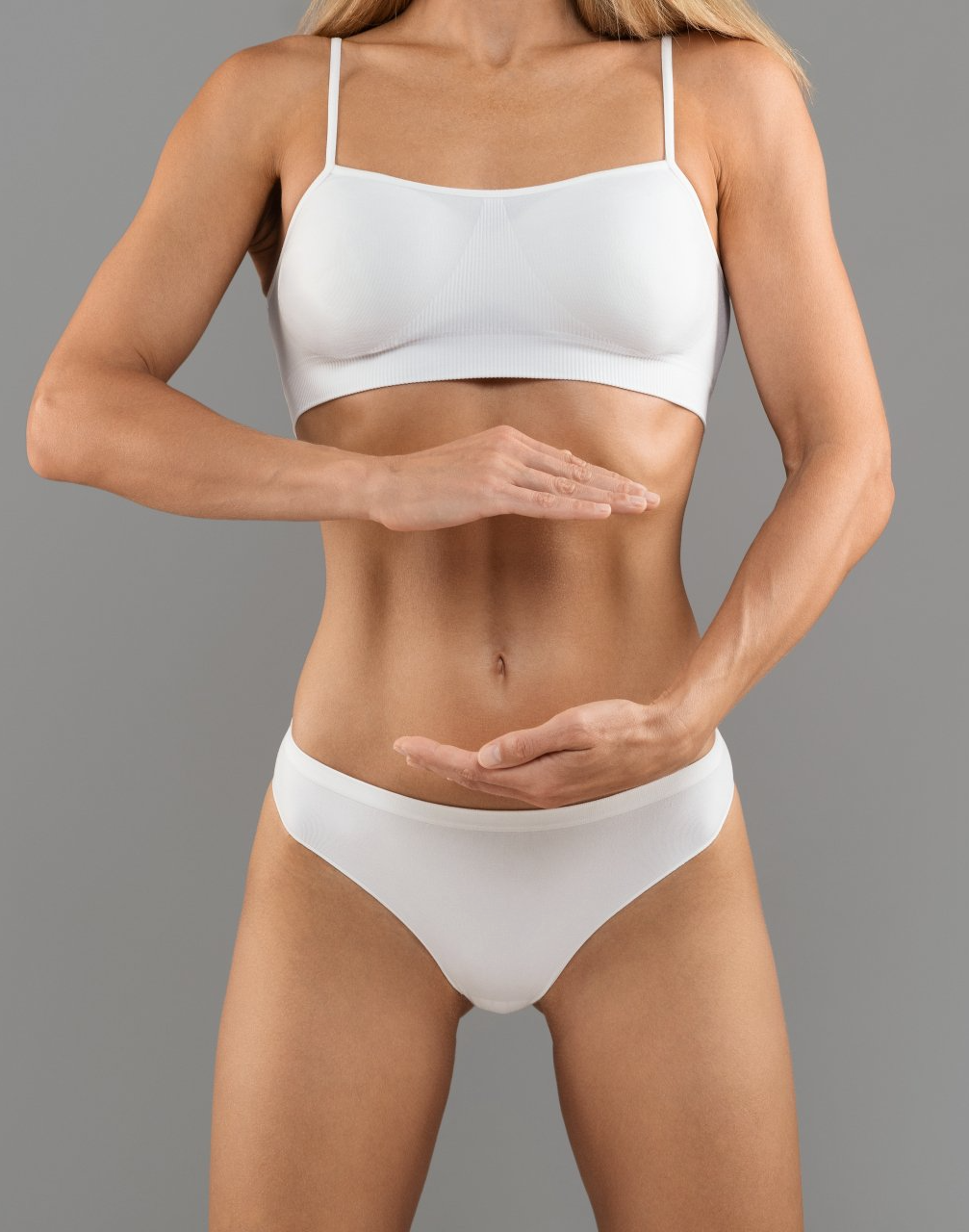 Woman in white underwear and top, hands framing her torso. Gray background.
