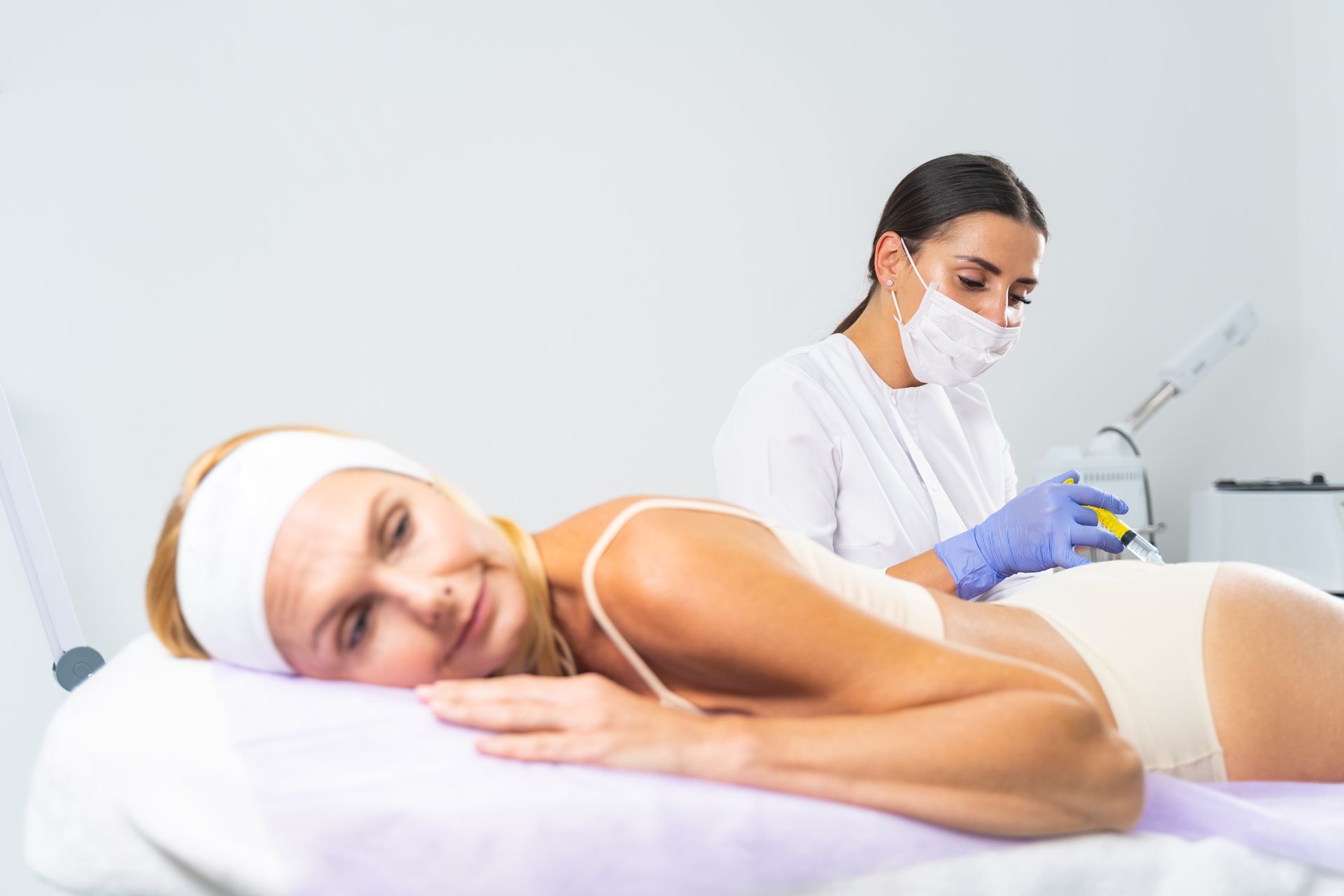 Woman receiving a back treatment in a medical setting, attended by a masked healthcare professional.