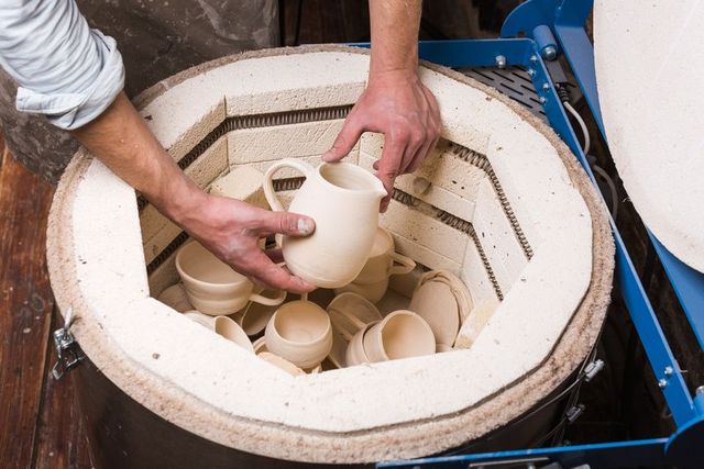 A person is putting a cup into a kiln filled with cups.