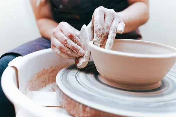 A woman is making a bowl on a pottery wheel.