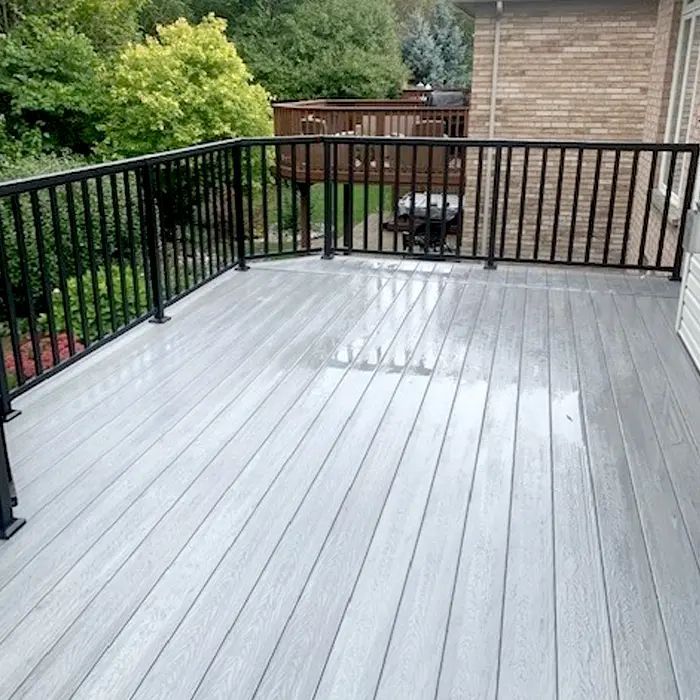 Empty gray deck with black railings overlooking a backyard and house.