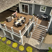 Wooden backyard deck with dining table, chairs, grill, and stairs leading to a house entrance.