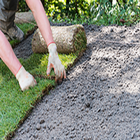 Gloved hands smoothing the edge between green grass and a freshly laid gravel path