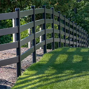Black rail fence along a grassy path with sunlight and trees in the background