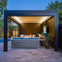 Modern backyard patio cabana with a lit ceiling, sectional sofa, potted plants, and TV at dusk