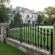 Black wrought-iron gate before a large white house with manicured lawn and trees