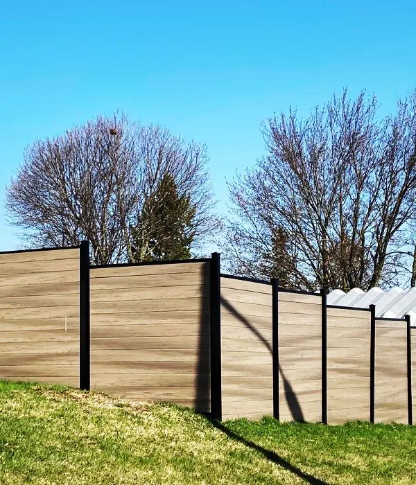 Wooden privacy fence with black posts along a grassy slope under a clear blue sky