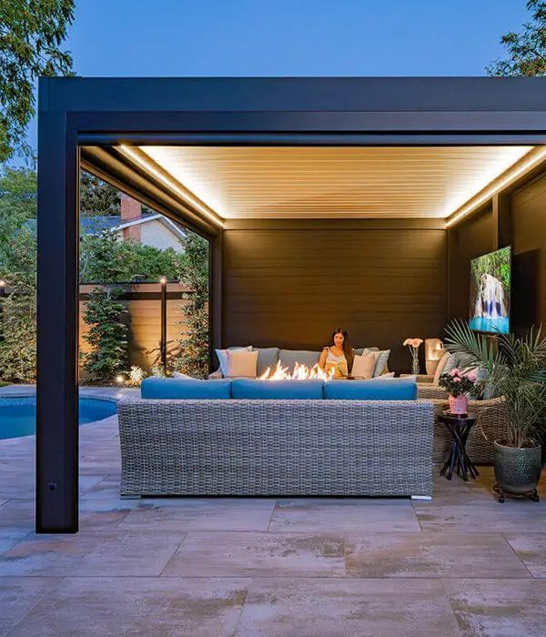 Covered patio lounge with sectional sofa, warm lighting, and a poolside view at dusk