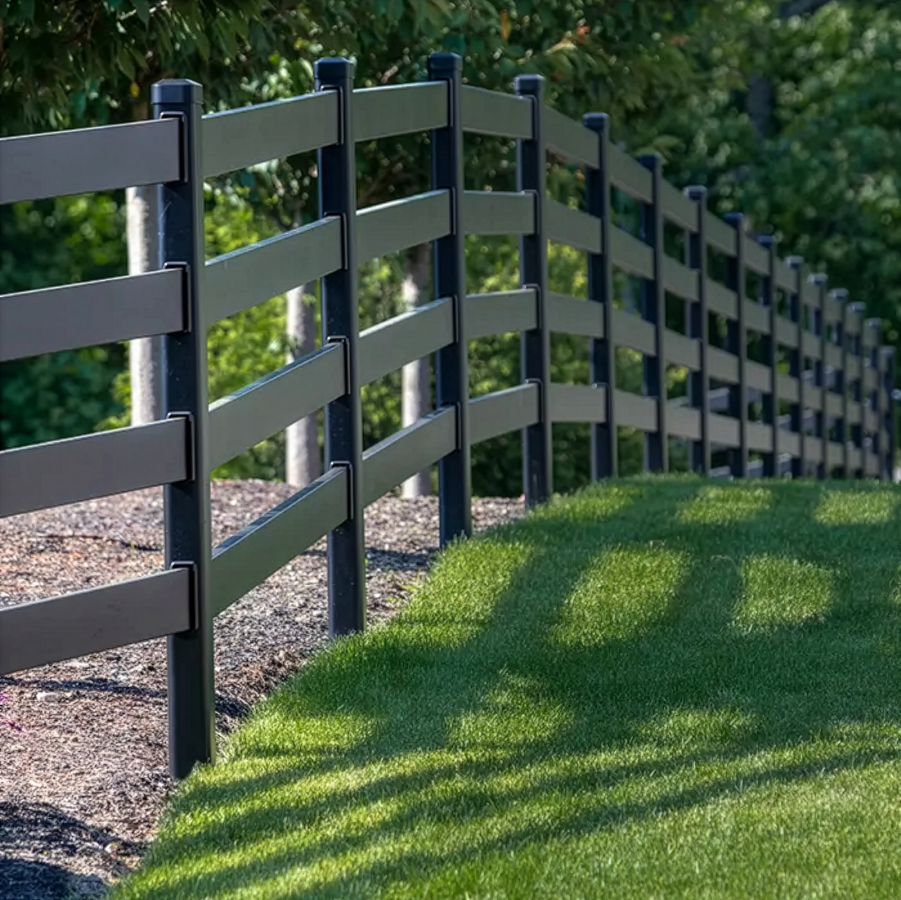 Black wooden fence along a grassy path with sunlight and tree shadows