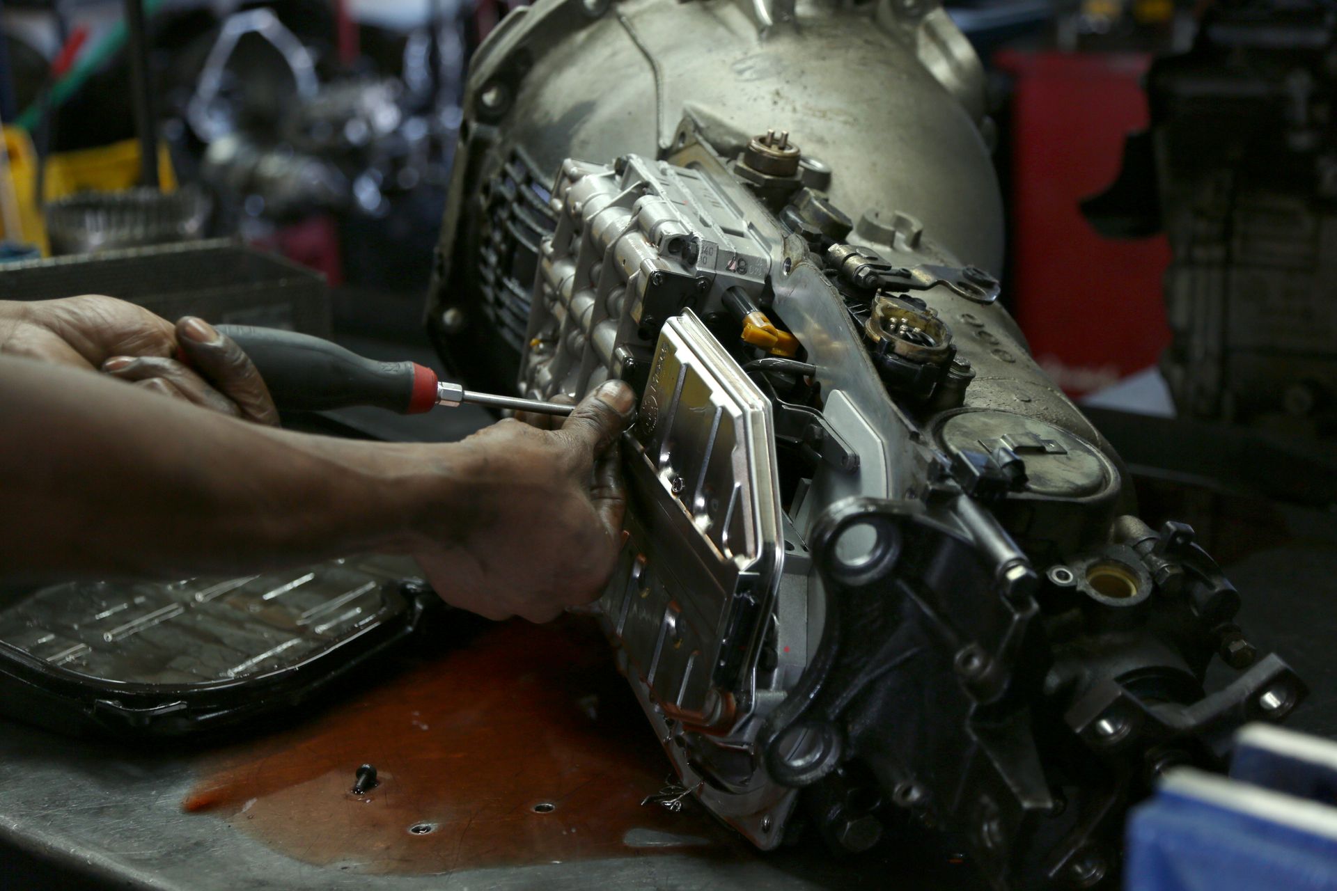 Close-up of a mechanic working in automatic transmissions, using a tool in a garage setting.